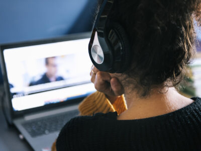 rear view of a woman with headphones watching a movie on laptop at home, technology and entertainment concept, selective focus