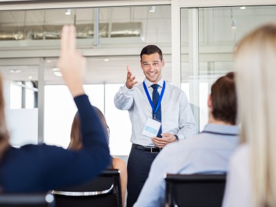 Businessman in seminar pointing towards woman raising hand to say a question. Human resource manager training new company employees. Businesswoman raising hand at conference to answer a question.