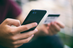 Close-up human hands with mobile phone and credit card. Person holds smartphone and bank card, closeup shot. On foreground male hands hold cell phone and card. Soft focus effect. Outdoors. In the city